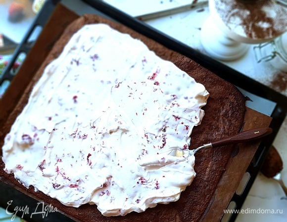 Выложить на корж взбитые сливки с малиной и свернуть в рулет при помощи коврика или бумаги.