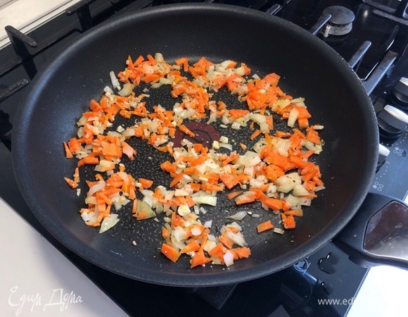 Оставшуюся половинку лука вместе с чесноком и морковкой мелко нарезать. Разогрейте на сковороде растительное масло и обжарьте на нем нарезанный лук (примерно 2–3 минуты). Добавьте к луку морковь и чеснок, перемешайте и обжаривайте еще 2 минуты.