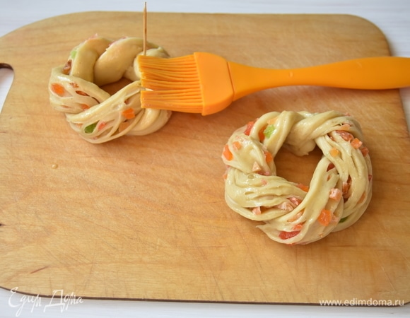 Готовые веночки оставить на 30–60 минут на расстойку, после чего смазать их смешанным с молоком яичным желтком. Выпекать пасхальные веночки в предварительно разогретой до 180°C духовке на противне, выстланном пергаментной бумагой, минут 20–25.