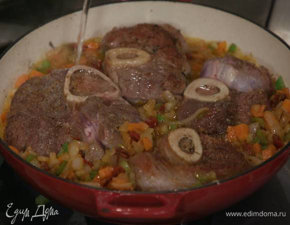 Выложить мясо на овощи, влить вино и дать алкоголю выпариться, затем влить горячий бульон, так чтобы мясо было практически покрыто, накрыть крышкой и тушить на очень маленьком огне до готовности.<br />
<br />
 