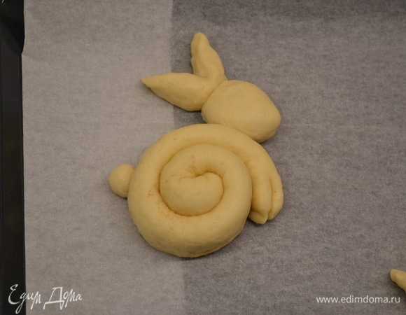 Формируем зайчиков: жгуты сворачиваем по спирали (получается тельце). Из остатков теста формируем небольшие хвостики и по два овала на каждого зайца. Один овал — это голова, второй надрезаем почти до конца — это уши. Все детали прикрепляем при помощи небольшого количества воды. Даем расстояться минут 25–30.