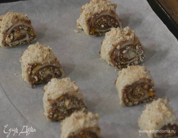 Сверху смазать рулет сливочным маслом, посыпать оставшейся ореховой крошкой и коричневым сахаром, нарезать небольшими кусочками и выложить их на противень, выстеленный бумагой для выпечки.