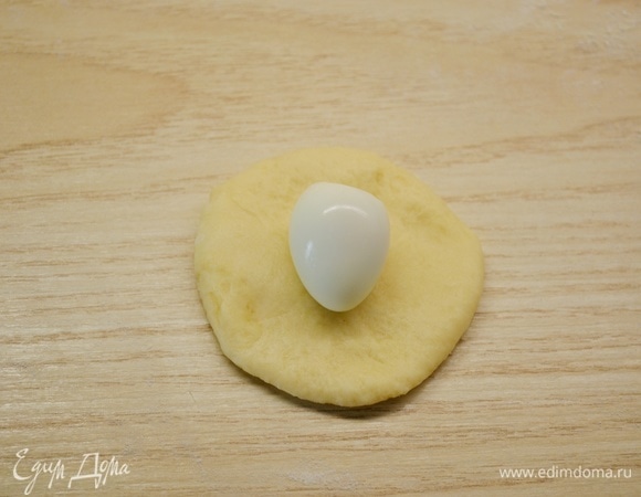 Тесто разделить на равные небольшие кусочки. Из каждого кусочка сформировать шарик, раскатать, на середину положить отварное очищенное перепелиное яйцо.