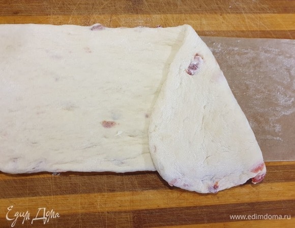 Отщипываем от теста небольшой кусочек, чтобы в дальнейшем сформировать дно кулича. Остальное тесто раскатываем и выкладываем на полоску пергамента, смазанного сливочным маслом. Ширина пергамента чуть выше формы для кулича.