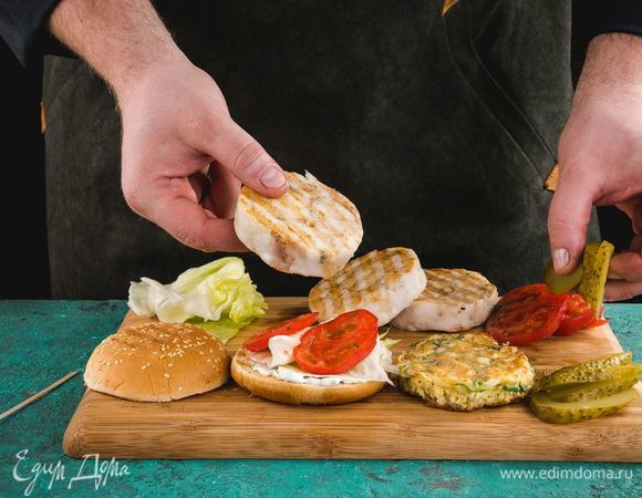 Смажьте одну часть булочки соусом и соберите бургер. На соус выложите листья салата, сверху — обжаренную рыбу. Затем положите нарезанные кружками помидоры и соленые огурцы.