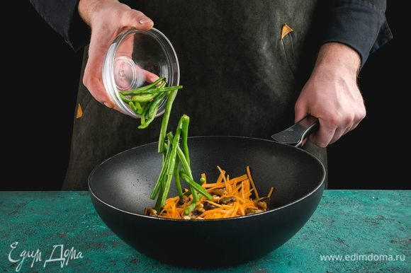 На сковороду с растительным маслом выложите шампиньоны, морковь и стручковую фасоль, обжарьте в течение нескольких минут.