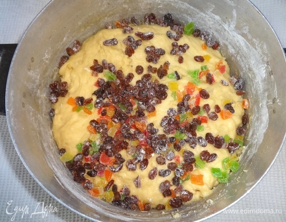 Подошедшее тесто обмять, добавить просушенный и обвалянный в муке изюм и цукаты. Распределить фрукты в тесте, хорошо вымесив. Поставить в теплое место подниматься.