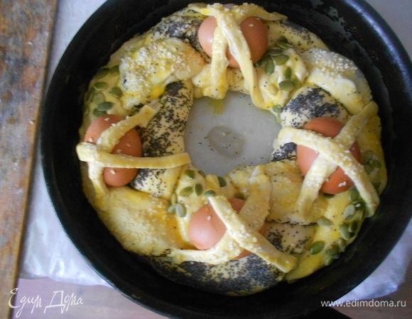 Аккуратно заплести косу и соединить края в кольцо. Выложить в форму, смазанную растительным маслом. Сырые яйца тщательно вымыть, обсушить. Отложенное тесто раскатать и вырезать из них полоски теста. Разместить 4 яйца по периметру косы и закрепить их крест накрест полосками из теста. Полоски тоже смазать яичным желтком и можно посыпать кунжутом. Оставить на расстойку на 30–35 минут.