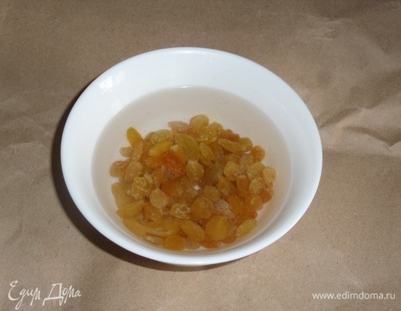 Изюм промываем, выкладываем в чашку. Заливаем изюм горячей водой и оставляем на 5 минут. Затем воду сливаем.