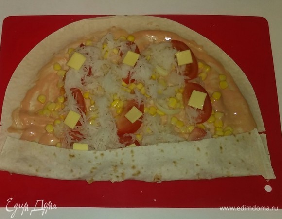 Когда все ингредиенты выложены на лаваш, начинаем его сворачивать и вначале загибаем лаваш снизу где-то на 2 сантиметра. Со второй частью лаваша поступаем так же.