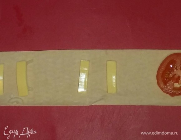 Берем одну полоску лаваша и раскладываем на ней кружок помидора, затем — полоски сыра, затем — полоски сыра с луком. С остальными полосками лаваша поступаем так же.