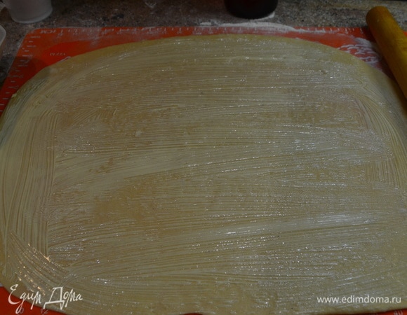 Тесто должно оставаться мягким, приятным в работе. Немного подсыпать стол мукой для формирования кулича. Разделите готовое тесто на 3 части. Раскатайте его в прямоугольный пласт толщиной около 3–4 мм. Смазать маслом, посыпать маком, изюмом, орехами, сахаром.