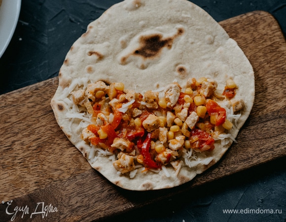 Выкладываем начинку и снова равномерно распределяем по половине лепешки. Посыпаем на начинку еще немного сыра сверху.