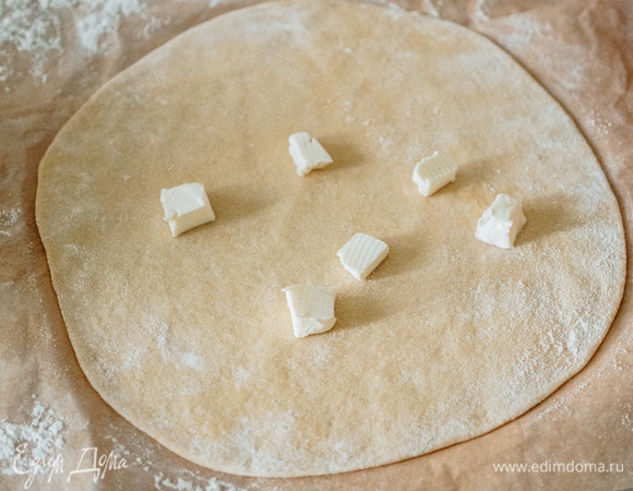 Подошедшее тесто аккуратно разделить на три равные части. Каждую часть раскатать. На раскатанный пласт теста нанести руками сливочное масло.