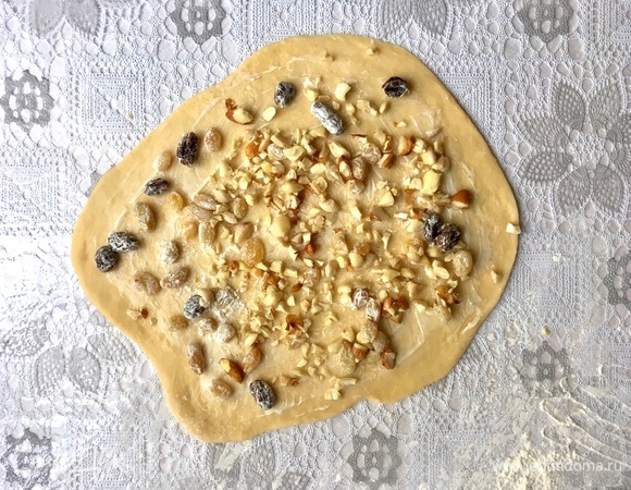 Раскатать каждую часть на припыленной мукой поверхности. Смазать размягченным сливочным маслом и распределить порубленные орехи и изюм.