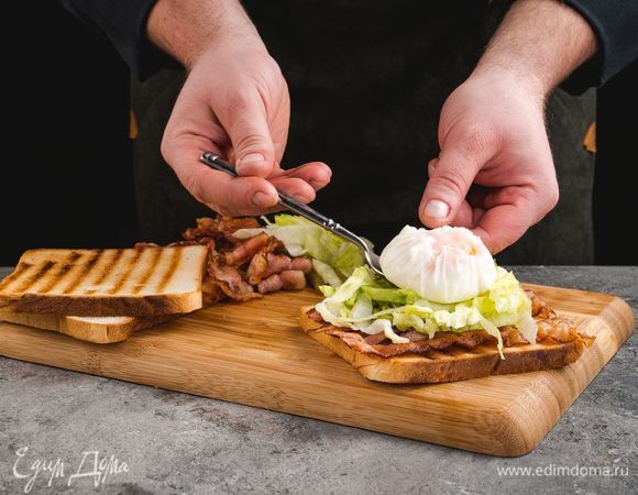На тосты выложите кусочки бекона, салат айсберг, сверху — яйца пашот и посыпьте тертым сыром.