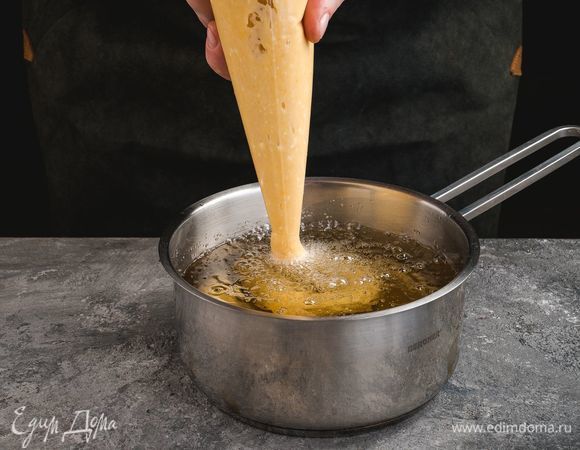 Тесто переложите в кондитерский мешок. Выдавливайте в горячее масло тесто произвольной формы. Обжарьте пончики в кипящем масле до золотистого цвета.