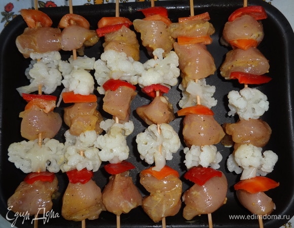 На деревянные палочки нанизывать, чередуя, кусочки курицы, перца и соцветия цветной капусты. Выложить шампуры с шашлыком на бортики противня или сковороды. Поставить противень в духовку, разогретую до 180°C, на 15–20 мин.
