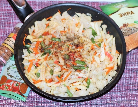 Добавьте очищенные и порезанные соломкой яблоки, лук, цветную капусту со стручковой фасолью. Всыпьте специи, посолите и поперчите. Перемешайте и тушите еще 2–3 минуты.