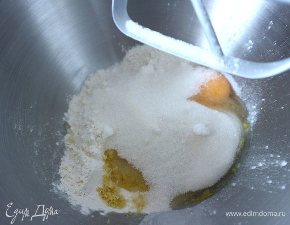 Натереть на мелкой терке цедру 1 лимона. В чашу комбайна поместить часть муки с разрыхлителем (примерно 1/3 часть), всю цедру, 1 яйцо, часть йогурта, сахара, масла, перемешать на небольшой скорости.