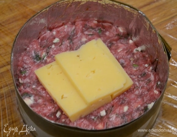 Готовим котлеты: укроп мелко нарезаем. Холодное сливочное масло натираем на крупной терке. Фарш, соль, перец, укроп и сливочное масло тщательно вымешиваем. Разделочную доску выстилаем пищевой пленкой. На нее ставим кулинарное кольцо, в кольцо выкладываем немного фарша, утрамбовываем, кладем пару кусочков сыра и сверху — опять немного фарша.