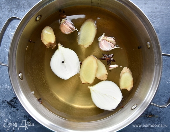 В кастрюлю влить воду. Добавить репчатый лук, чеснок, несколько ломтиков имбиря, черный перец горошком, гвоздику, кардамон и бадьян. Влить соевый соус, посолить, всыпать сахар и довести до кипения.