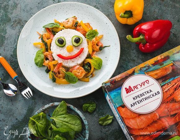 Вокруг риса выложите креветки со шпинатом и перцем. На рисе выложите рожицу с глазками из кружков огурца и маслины, носом из кусочка маслины и ртом из ломтика болгарского перца. Этот веселый обед точно понравится вашему малышу!