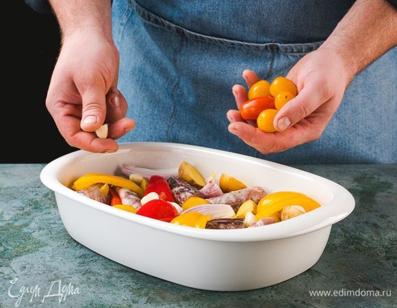 Выложите картофель, лук, перец и рыбу на смазанный маслом противень, сверху положите черри и разрезанные пополам зубчики чеснока. Сверху полейте оливковым маслом. Выпекайте 25–30 минут при температуре 200°C.