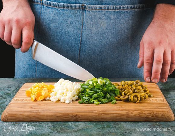 Яйца отварите вкрутую. Остудите и очистите. Нарежьте крупно зеленый лук, оливки. Белки и желтки нарежьте по отдельности.