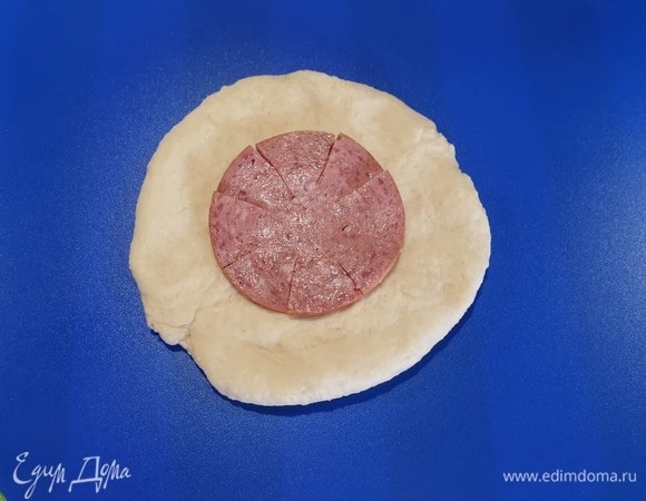 Каждую заготовку несильно раскатываем. Делаем надрезы на салями, чтобы в итоге пицца получилась идеально круглой. Кладем салями в центр.