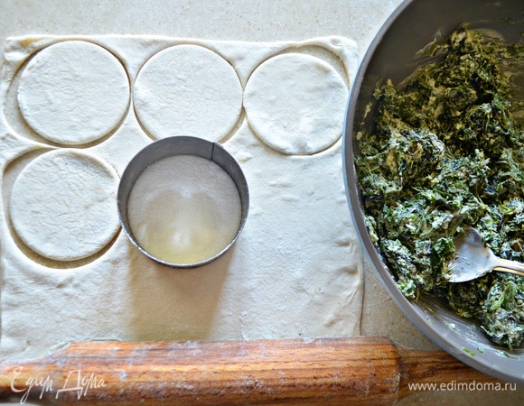 Тесто разморозьте при комнатной температуре и раскатайте на посыпанной мукой поверхности. С помощью кулинарного кольца вырежьте небольшие круги. Из 1 пласта теста получилось 9 шт. Остатки теста соберите в шар и снова раскатайте. Из всего теста получается порядка 27 заготовок для пирожков.