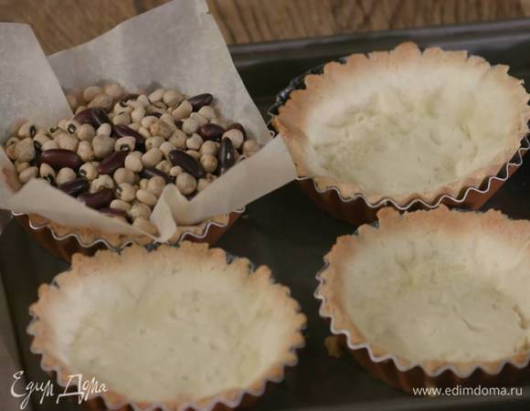 В формочки с охлажденным тестом вложить квадратики пищевой бумаги, всыпать любые бобовые и выпекать в разогретой духовке 10 минут, затем снять бумагу с бобовыми, понизить температуру духовки до 170°С и выпекать тарталетки еще 5 минут.