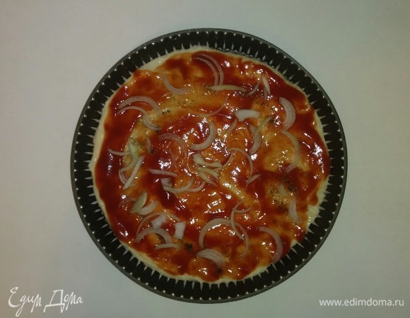 Форму для пиццы смазываем оливковым маслом и посыпаем мукой. Раскатываем тесто по форме. Затем смазываем его протертыми помидорами, посыпаем приправой для пиццы и выкладываем нарезанный репчатый лук.