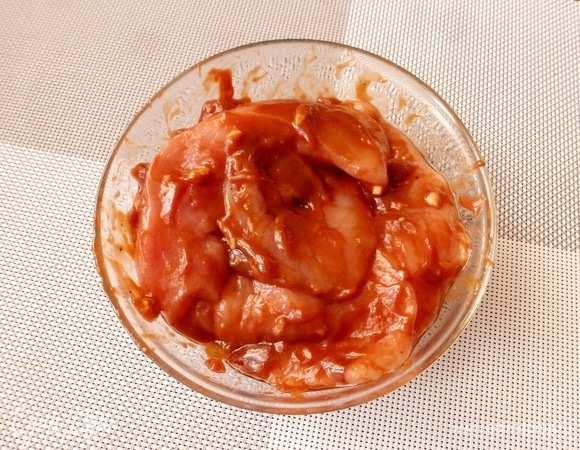 Для маринада я взяла кетчуп гриль для барбекю, у него вкус дымка (можно взять и другой вкусный кетчуп). Выдавить в кетчуп чеснок, добавить щепотку сахара, соль и перец, влить немного растительного масла. Все перемешать. Замариновать куриные кусочки на 1 час.