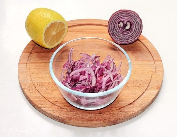 Очищенный красный лук нарезаем тонкими полукольцами и заливаем горячей водой. Добавляем 1 ст. л. лимонного сока и оставляем мариноваться на 5–10 минут. Затем воду сливаем, лук охлаждаем.