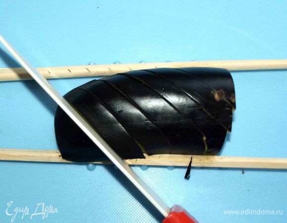 Четвертинку баклажана фиксируем китайскими палочками (это будет наш ограничитель) и надрезаем баклажан наискосок в одну сторону.