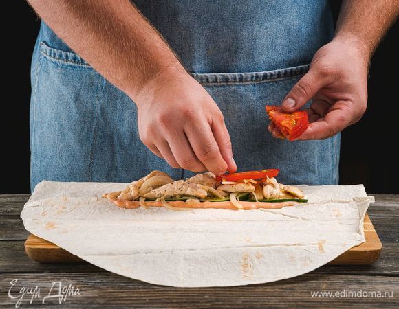 Каждый лист лаваша разрежьте пополам, смажьте соусом. Выложите на один край лаваша нарезанные огурцы, обжаренное куриное филе и помидоры.
