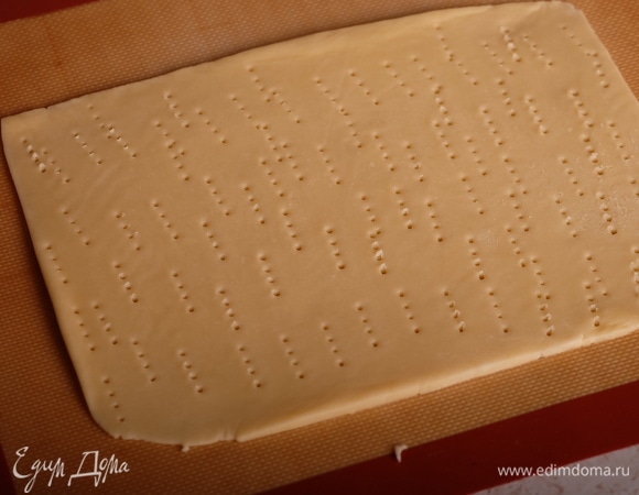 Духовку разогреть до 200°C. Охлажденное тесто раскатать между двумя листами пергамента в прямоугольный пласт толщиной 3–4 мм. Наколоть вилкой.