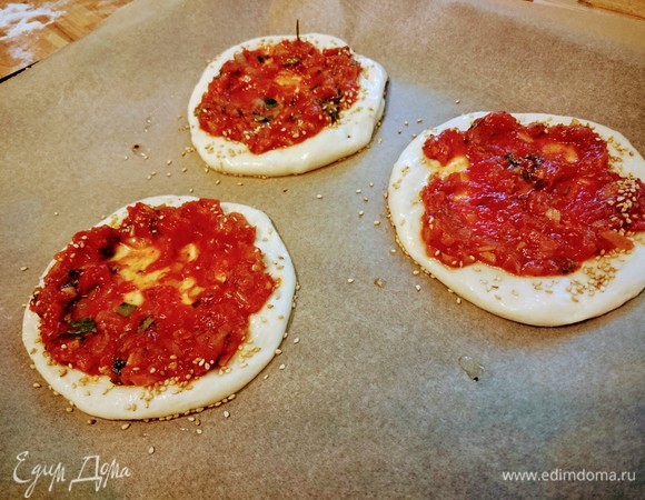 Через 20 минут слегка смазанными маслом руками, приминая тесто кончиками пальцев, придайте ему форму лепешек. Распределите соус по лепешкам, оставляя пустым край. Его смажьте маслом и посыпьте кунжутом. Запекайте в заранее разогретой до 180°C духовке 15 минут. Для равномерного запекания я меняла противни местами.