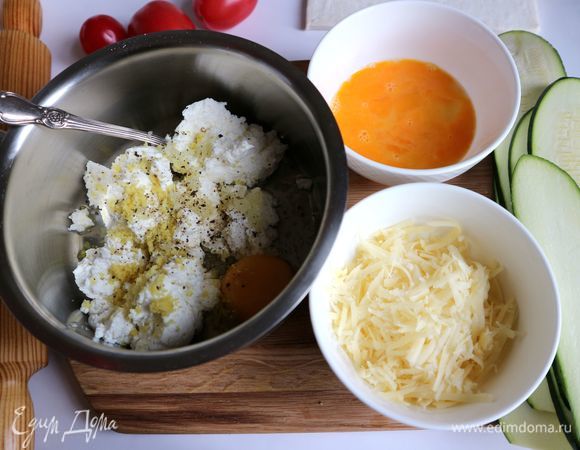 Цукини нарезать вдоль на пластины, смазать оливковым маслом, посолить. Чеснок почистить, выдавить через пресс для чеснока, добавить к творогу (использовала творог из пачки, а не мягкий) и сливочному творожному сыру, с лимона снять цедру с помощью мелкой терки, добавить к смеси, добавить яйцо, посолить, поперчить, добавить орегано, перемешать. Второе яйцо разбить в отдельную посуду, перемешать венчиком, половину от него добавить к смеси, вторую половину яйца оставить для смазывания бортиков из теста. Сыр натереть на крупной терке.