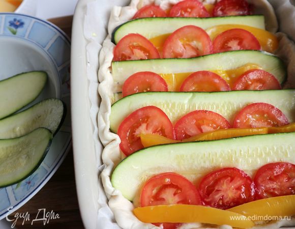 Сверху поместить овощи, чередуя пластины цукини, полоски желтого болгарского перца, колечки помидоров. Размещать таким образом, чтобы одна часть овощей заходила на другую. Смазать кисточкой бортики из теста взбитым яйцом. Отправить в духовку на 40 минут.