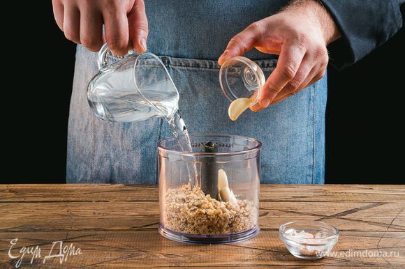 В чашу блендера положите измельченные орехи, соль, чеснок и влейте воду.