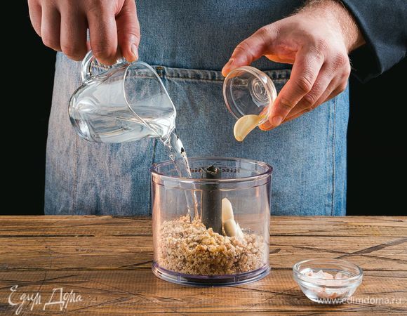 В чашу блендера положите измельченные орехи, соль, чеснок и влейте воду.