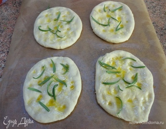 Пекарскую бумагу смажьте маслом. Тесто разделите на 4 части и руками сформируйте лепешки на этом листе. Пальцами сделайте внизу углубления и полейте оставшимся процеженным чесночным маслом. По желанию уложите по несколько листочков розмарина и посыпьте крупной солью. Теперь духовку вместе с противнем, на котором будете выпекать фокаччу, включите на разогрев до 240°C. Пока она разогреется, фокачча немного поднимется.