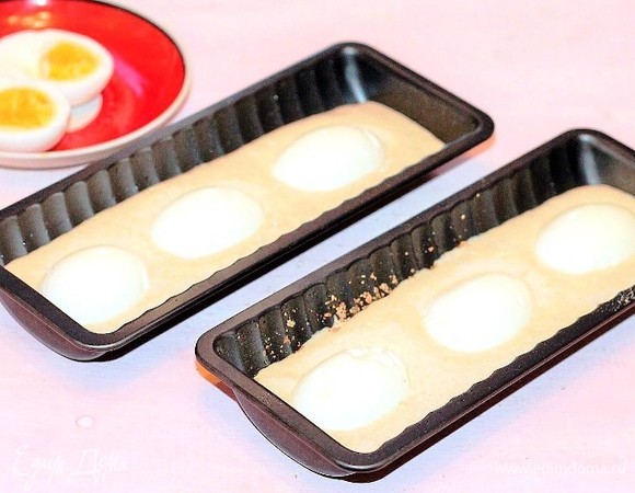 Выкладываем 1/2 часть теста и разравниваем силиконовой лопаткой. Кладем в каждую формочку по 3 половинки вареных яиц и топим их в тесте. У меня яйца отварены не вкрутую: белок отварен полностью, а желток — наполовину. Если у вас не вышло так отварить яйца, то лучше натрите их на крупной терке и добавьте в начинку. Почему? Вареные, крупно нарезанные яйца после выпечки в тесте становятся жесткими, особенно белок.