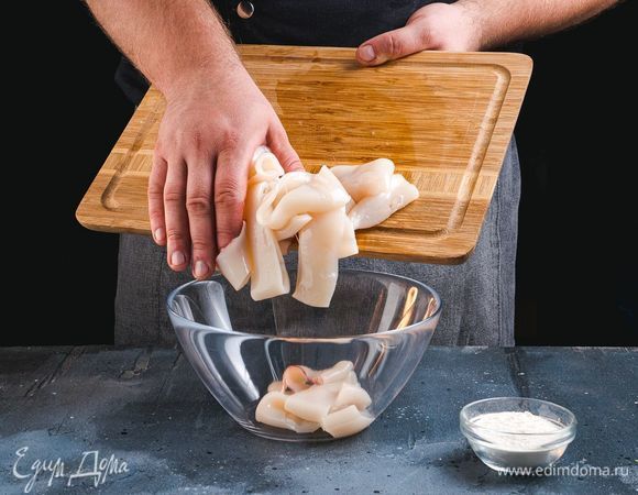 Разрежьте кальмары на три-четыре части. Выложите их в глубокую чашку, посолите, поперчите и тщательно перемешайте. Затем добавьте муку, еще раз перемешайте.