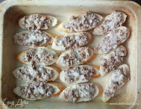 Тонкий батон (багет) нарезать кусочками толщиной 1 см (10–12 кусочков), уложить на противень. На батон распределить получившуюся начинку.