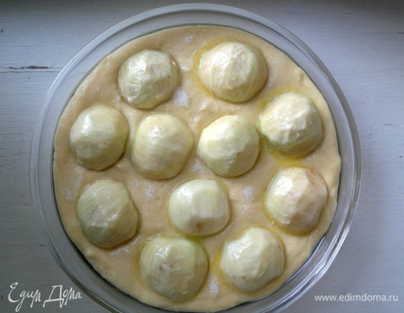 Выложить половинки яблок на пирог, слегка вдавливая их в тесто. Растопить 25 г сливочного масла, смазать им яблоки. Промежутки теста между яблоками посыпать сахаром. Поставить форму с пирогом в духовку, разогретую до 180°C, на 30–35 минут. Готовность проверять деревянной палочкой: если выходит сухой из пирога, значит, пирог готов.