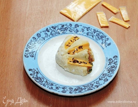 Украшаем заготовки булочек полосками плавленого сыра и посыпаем тмином. Плавленый сыр можно заменить на тертый твердый сыр, а тмин — на черный кунжут. Но тмин очень ароматный.