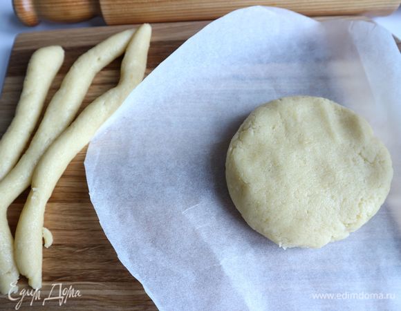 Вырезать круг из бумаги для выпечки по размеру донышка формы. От теста отделить часть на бортики, остальное раскатать на бумаге для выпечки с помощью скалки, чуть посыпанной мукой. Вырезать полосу бумаги для бортиков. Сделать бортики из теста.